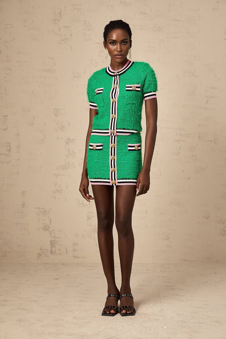 Young woman wearing a green knitted top and matching skirt set standing against a plain background