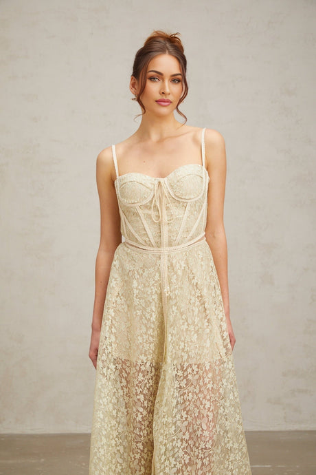 Young woman wearing a light green midi dress with floral embroidery details standing in front of a plain background