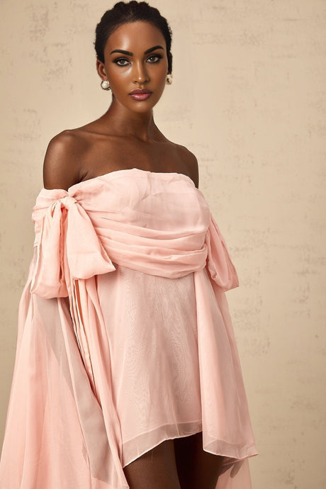 Young woman wearing a light pink mini dress with bow detail and draped fabric design