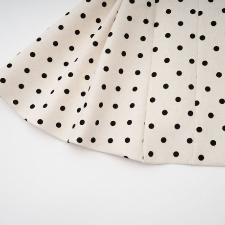 Young woman wearing a lightcolored polka dot mini dress with puff sleeves and a fitted waist standing against a neutral background