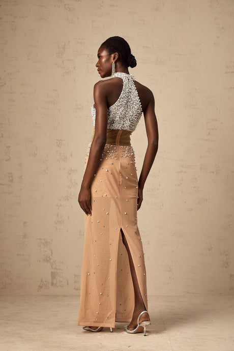 Young woman wearing a long flowy white semi sheer maxi dress with faux pearl embellishments walking on a beach