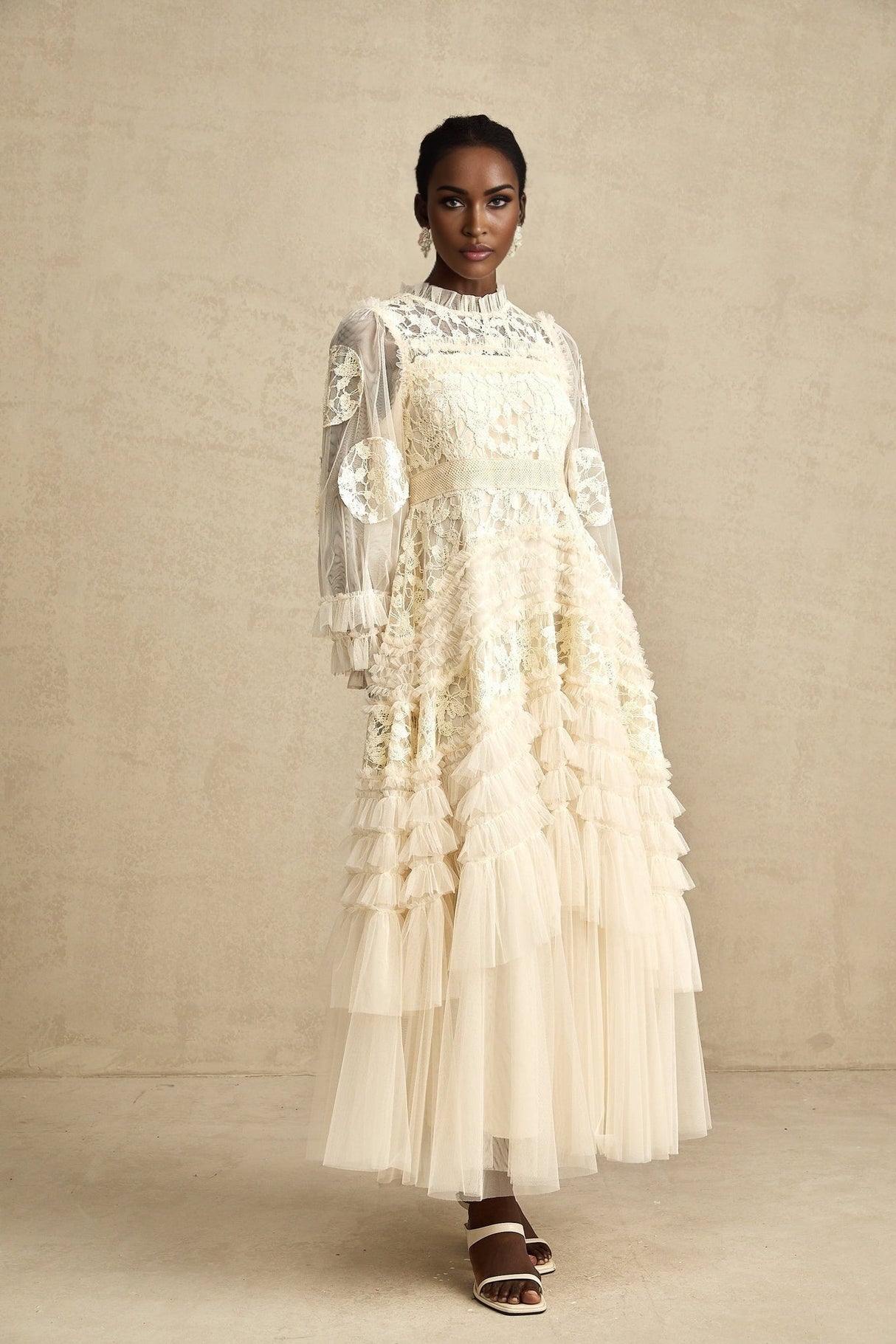Young woman wearing a long white tulle maxi dress with floral embroidery and layered skirt standing in garden setting