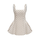 Young woman wearing a neutral colored polka dot mini dress with puff sleeves and a fitted waist standing against a plain background