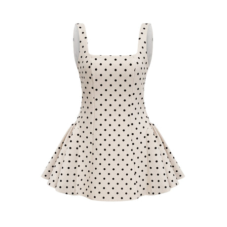 Young woman wearing a neutral colored polka dot mini dress with puff sleeves and a fitted waist standing against a plain background