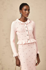 Young woman wearing a pink argyle pattern knitted cardigan with matching skirt set against a plain background