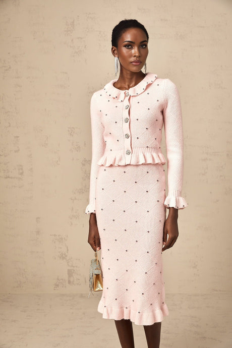 Young woman wearing a pink argyle patterned knit cardigan and matching skirt set against a plain background