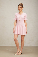 Young woman wearing a pink flared mini dress with a fine knit texture standing against a plain background