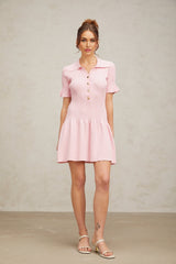 Young woman wearing a pink flared mini dress with fine knit fabric standing against a plain background