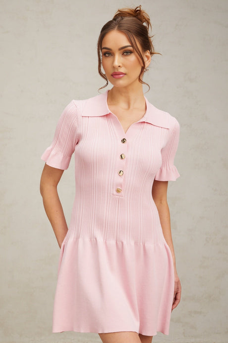 Young woman wearing a pink flared mini dress with fine knit texture standing against a plain background