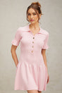 Young woman wearing a pink flared mini dress with fine knit texture standing against a plain background