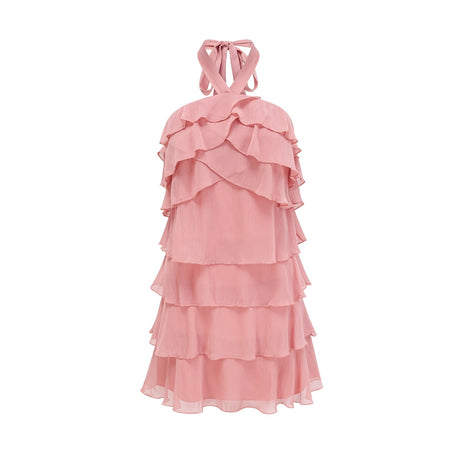 Young woman wearing a pink halterneck mini dress with tiered ruffles standing against a plain background