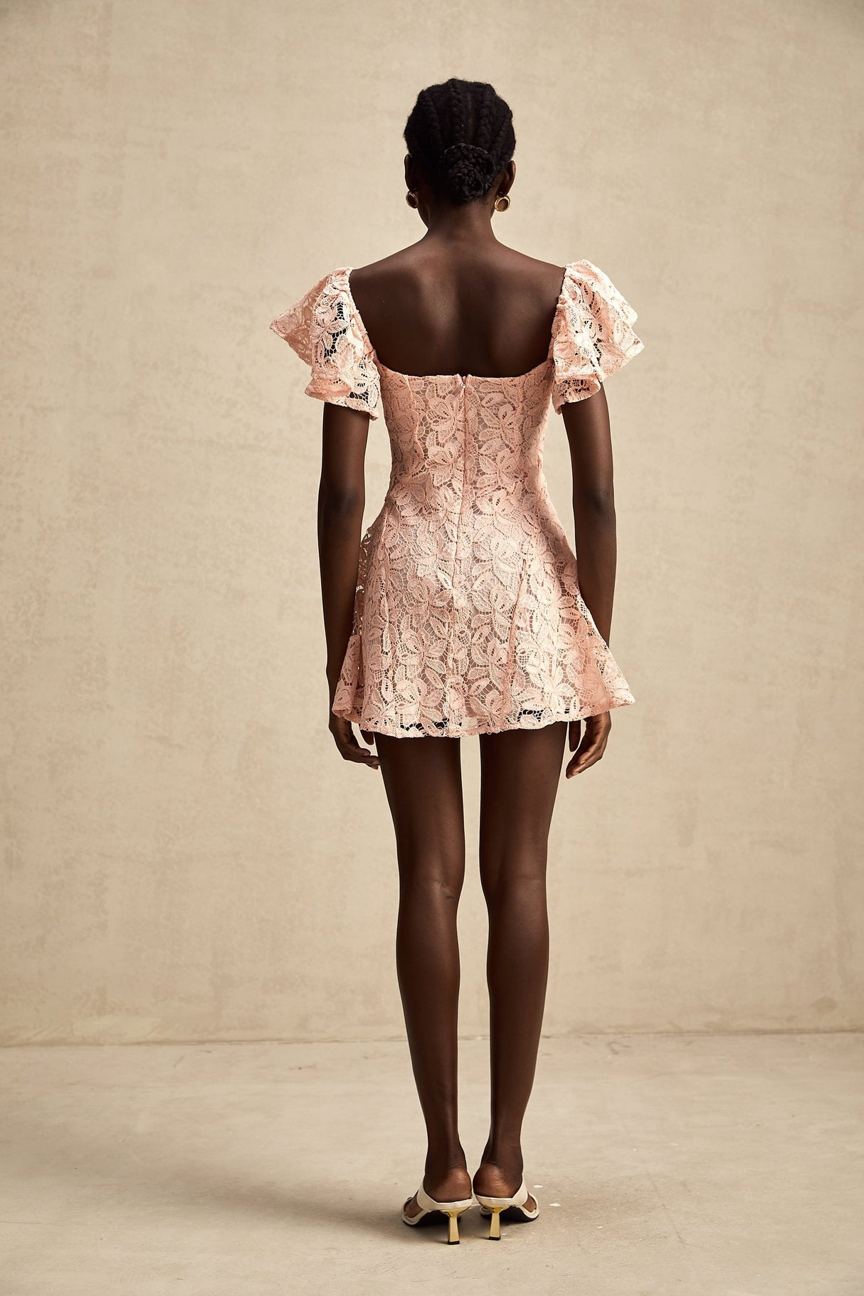 Young woman wearing a pink lace mini dress with flutter sleeves standing in a casual pose