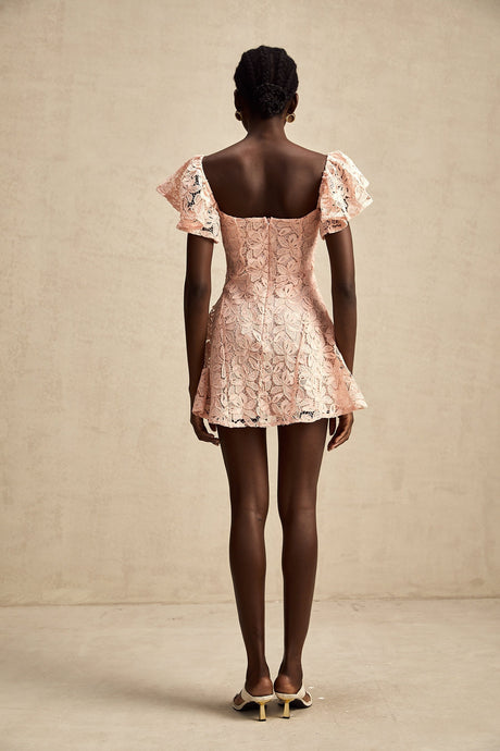 Young woman wearing a pink lace mini dress with flutter sleeves standing in a casual pose