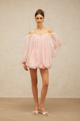 Young woman wearing a pink layered bubble tulle mini dress with a fitted bodice and voluminous skirt standing against a plain background
