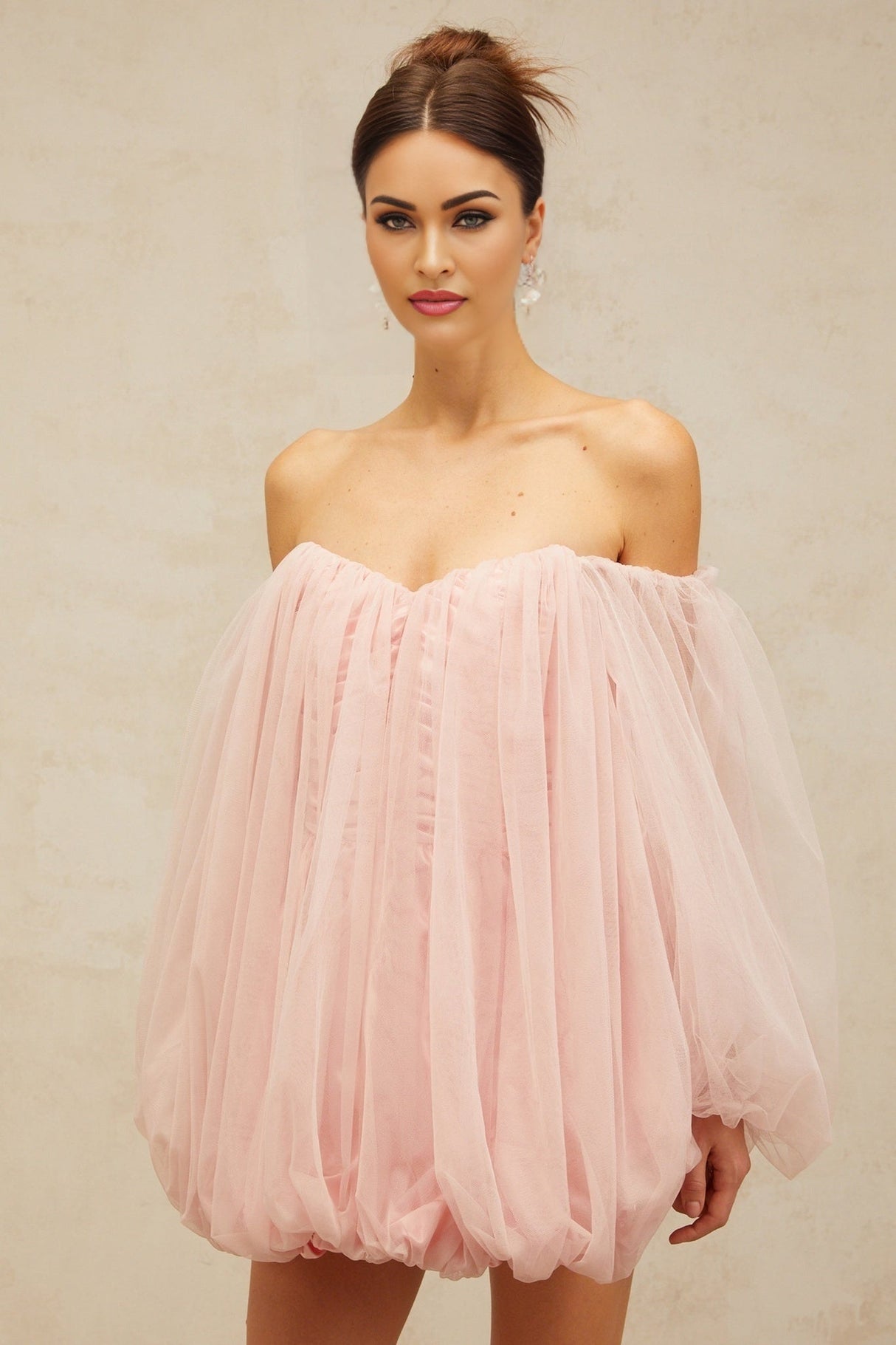 Young woman wearing a pink layered tulle mini dress with bubble sleeves standing against a plain background