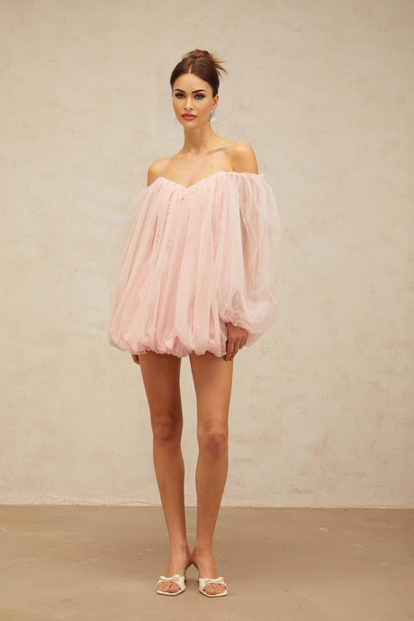 Young woman wearing a pink layered tulle mini dress with bubble sleeves standing against a plain background