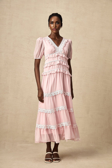 Young woman wearing a pink midi dress with ruffled tiers and a flowy silhouette standing against a plain background