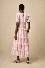 Young woman wearing a pink midi dress with tiered ruffles and a flowy silhouette standing against a plain background