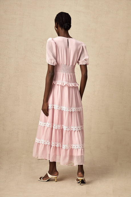 Young woman wearing a pink midi dress with tiered ruffles and a flowy silhouette standing against a plain background