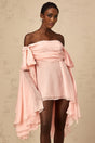 Young woman wearing a pink mini dress with bow detail and draped fabric standing against a plain background