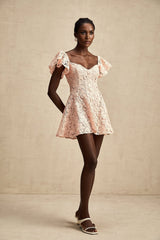 Young woman wearing a pink mini dress with flutter sleeves and lace detailing standing in a casual pose