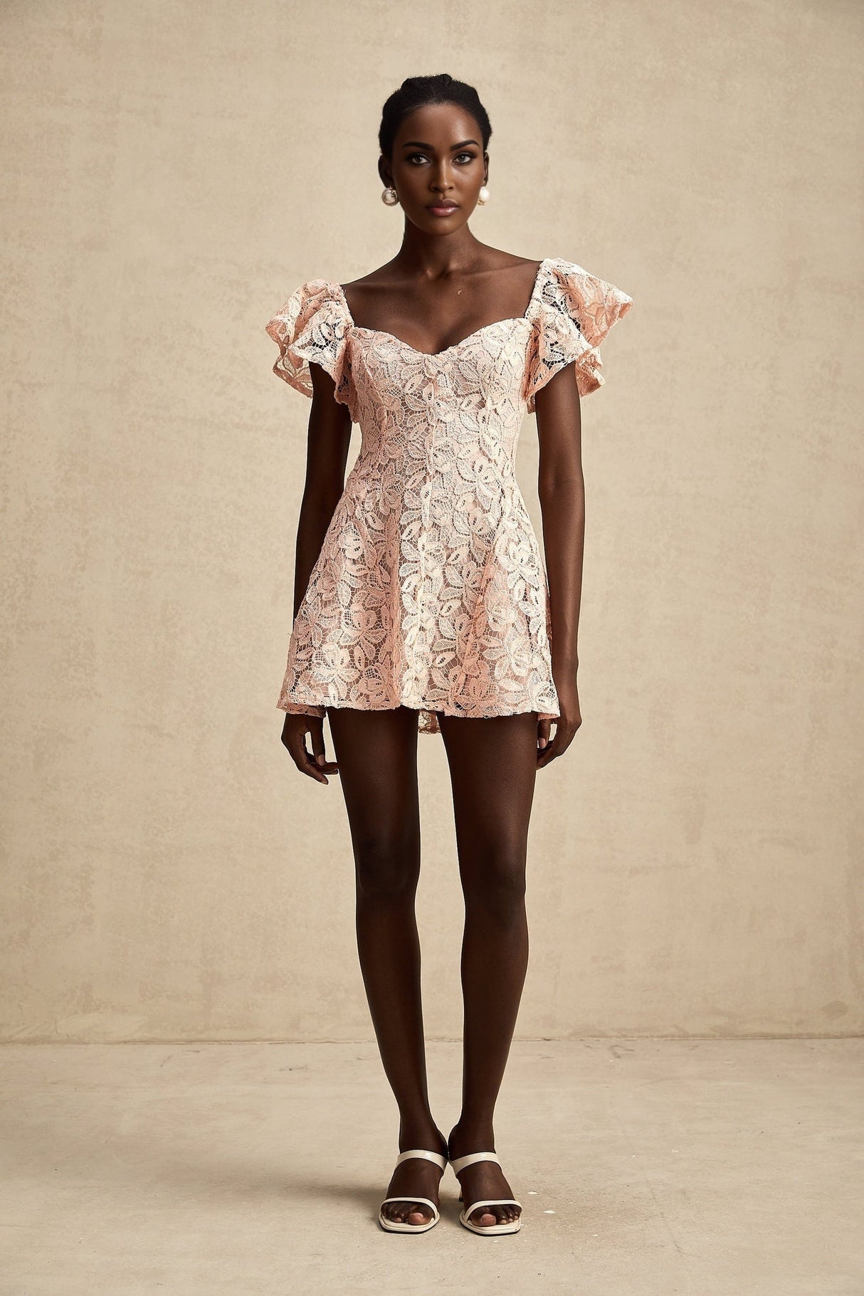 Young woman wearing a pink mini dress with flutter sleeves and lace detailing standing in a relaxed pose against a plain background