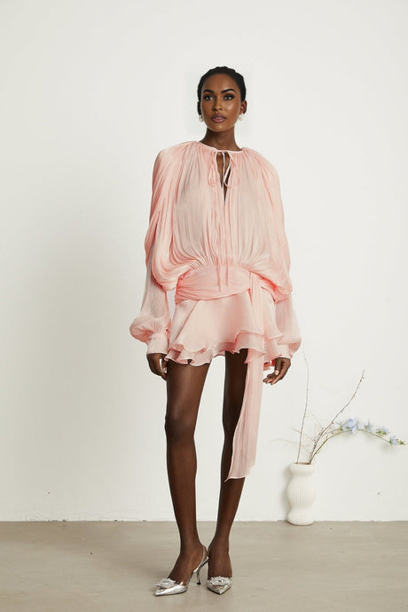 Young woman wearing a pink mini dress with full pleats and ruffled details standing in a casual pose