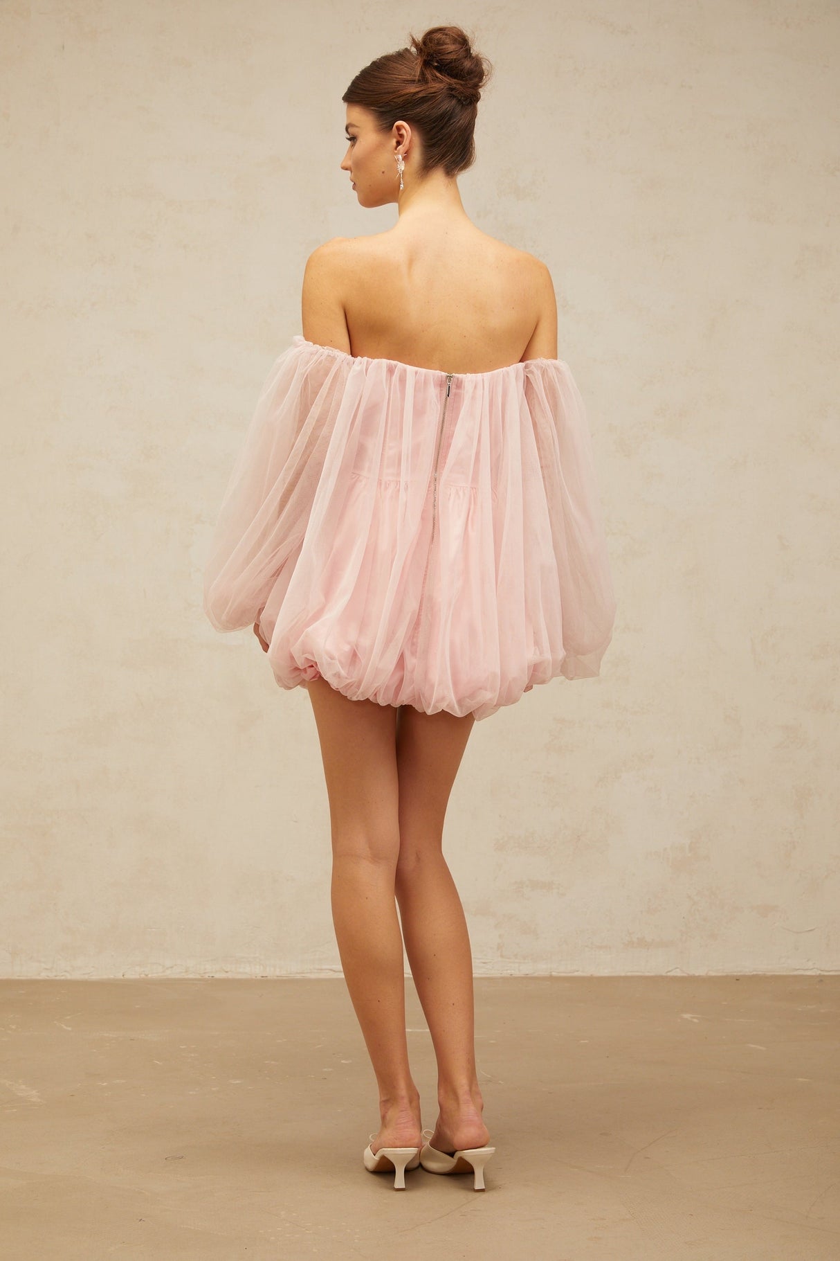 Young woman wearing a pink mini dress with layered bubble tulle skirt standing against a plain background