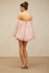 Young woman wearing a pink mini dress with layered bubble tulle skirt standing against a plain background