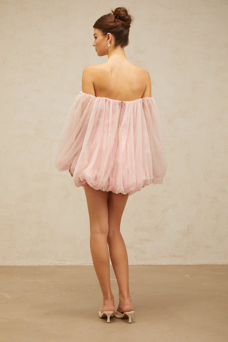 Young woman wearing a pink mini dress with layered bubble tulle skirt standing against a plain background