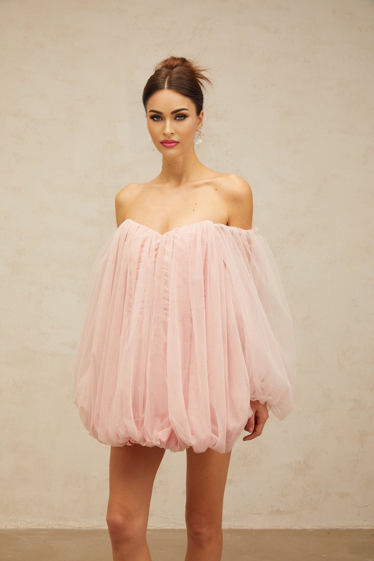 Young woman wearing a pink mini dress with layered bubble tulle skirt standing against a plain background