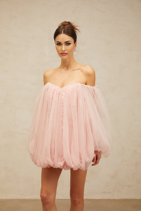 Young woman wearing a pink mini dress with layered bubble tulle skirt standing against a plain background