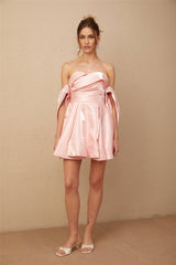 Young woman wearing a pink off shoulder mini dress with puff sleeves made of satin fabric