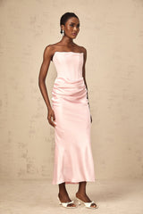 Young woman wearing a pink offshoulder maxi dress with flowing fabric standing in a garden setting