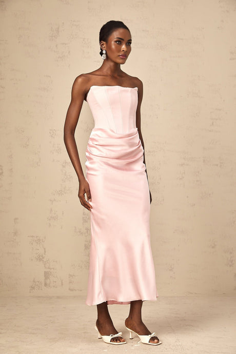 Young woman wearing a pink offshoulder maxi dress with flowing fabric standing in a garden setting