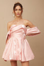 Young woman wearing a pink offshoulder mini dress with puff sleeves made of satin fabric