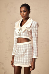 Young woman wearing a pink tweed jacket and matching skirt with a checkered pattern standing against a plain background