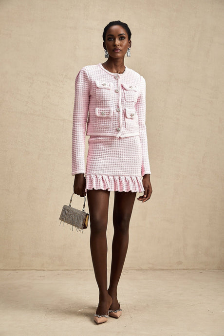 Young woman wearing a pink waffleknit jacket and matching skirt set standing against a plain background