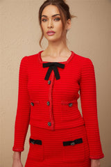 Young woman wearing a red braided waffle knit jacket and matching skirt set named Cynthia standing against a plain background