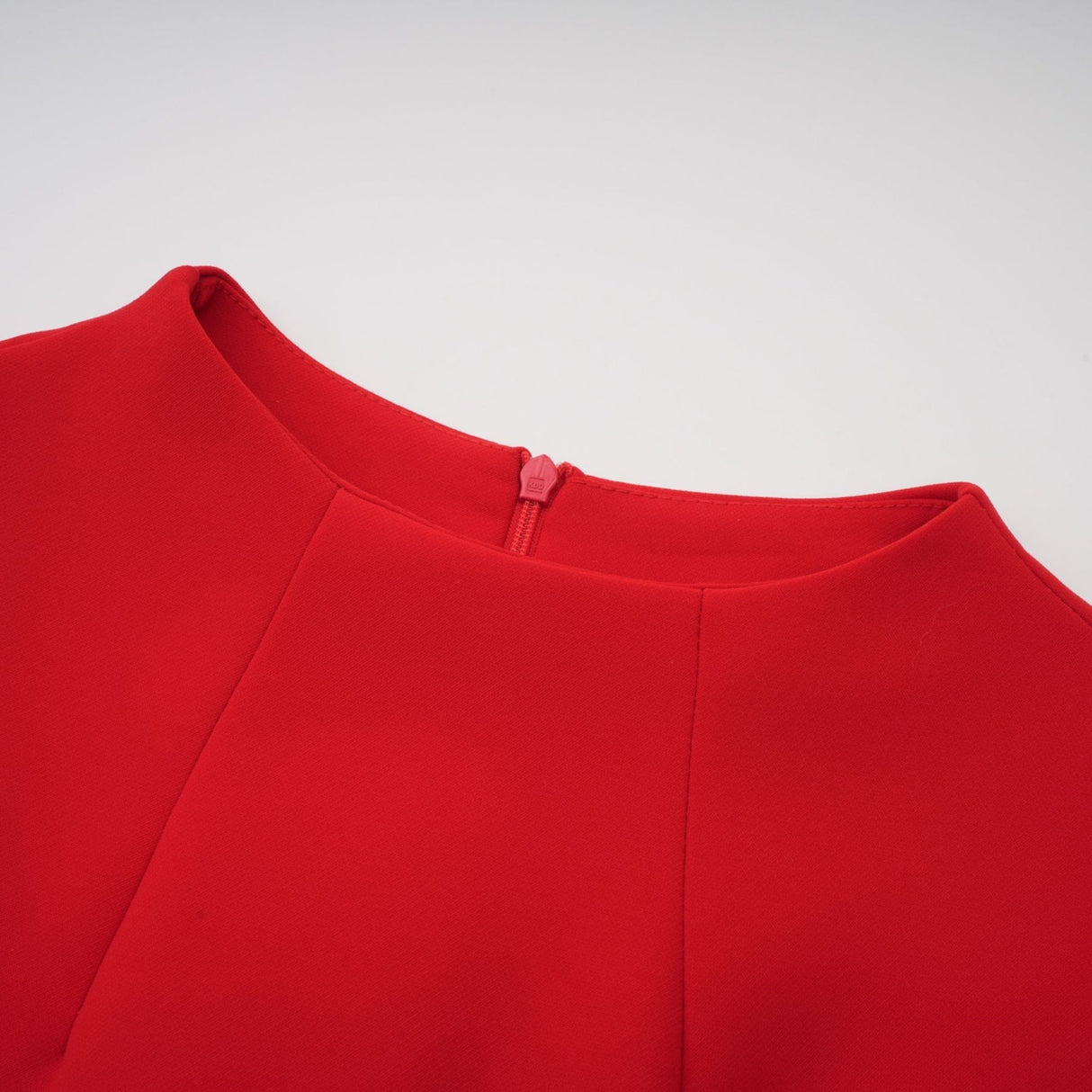 Young woman wearing a red mini dress with cap sleeves standing against a plain background