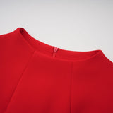 Young woman wearing a red mini dress with cap sleeves standing against a plain background