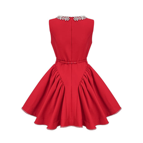 Young woman wearing a red pleated mini dress with embellishments standing in front of a plain background