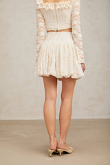 Young woman wearing a shimmering pleated mini skirt with sequin details standing against a plain background