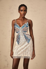 Young woman wearing a short beaded dress with butterfly designs standing in front of a white background