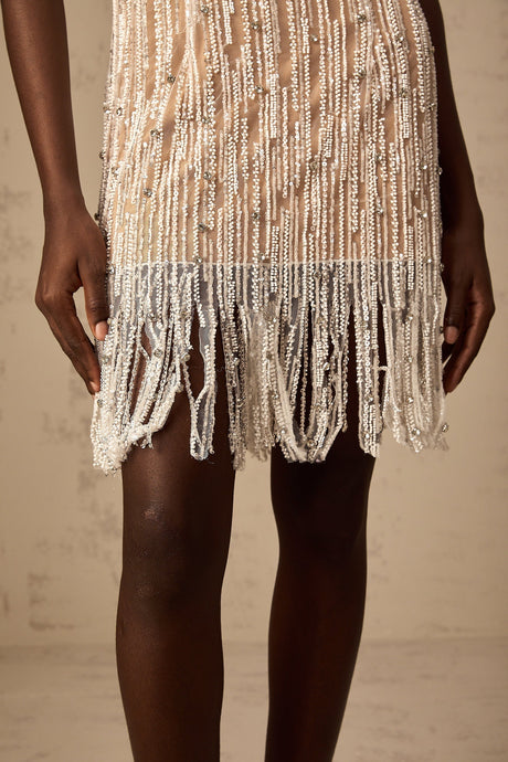 Young woman wearing a short black dress with sparkly embellishments and fringe details at the hem