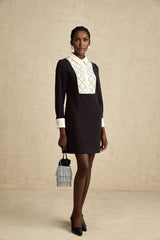 Young woman wearing a short embellished mini dress with contrasting colors and decorative details standing in a neutral background