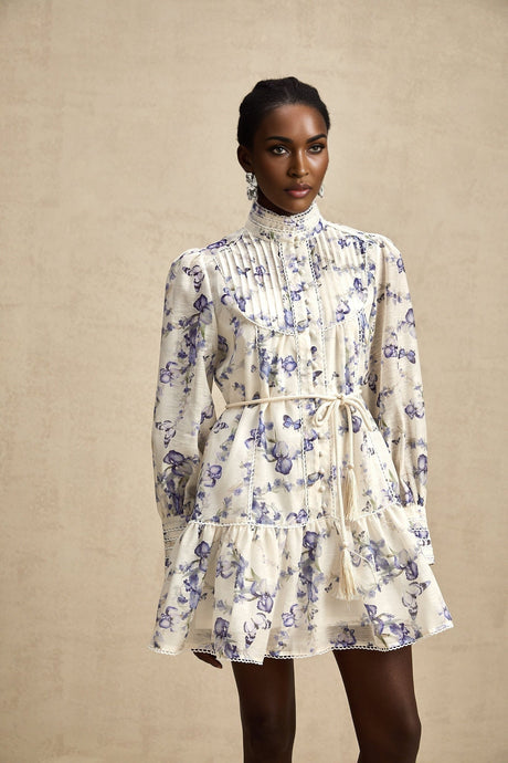 Young woman wearing a short flared chiffon dress with colorful floral print pattern and flowing sleeves standing in a natural outdoor setting