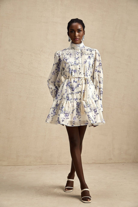 Young woman wearing a short flared chiffon dress with floral print pattern in pastel colors against a plain background