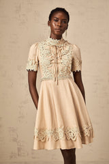 Young woman wearing a short flared dress with corded lace pattern and delicate straps standing against a plain background