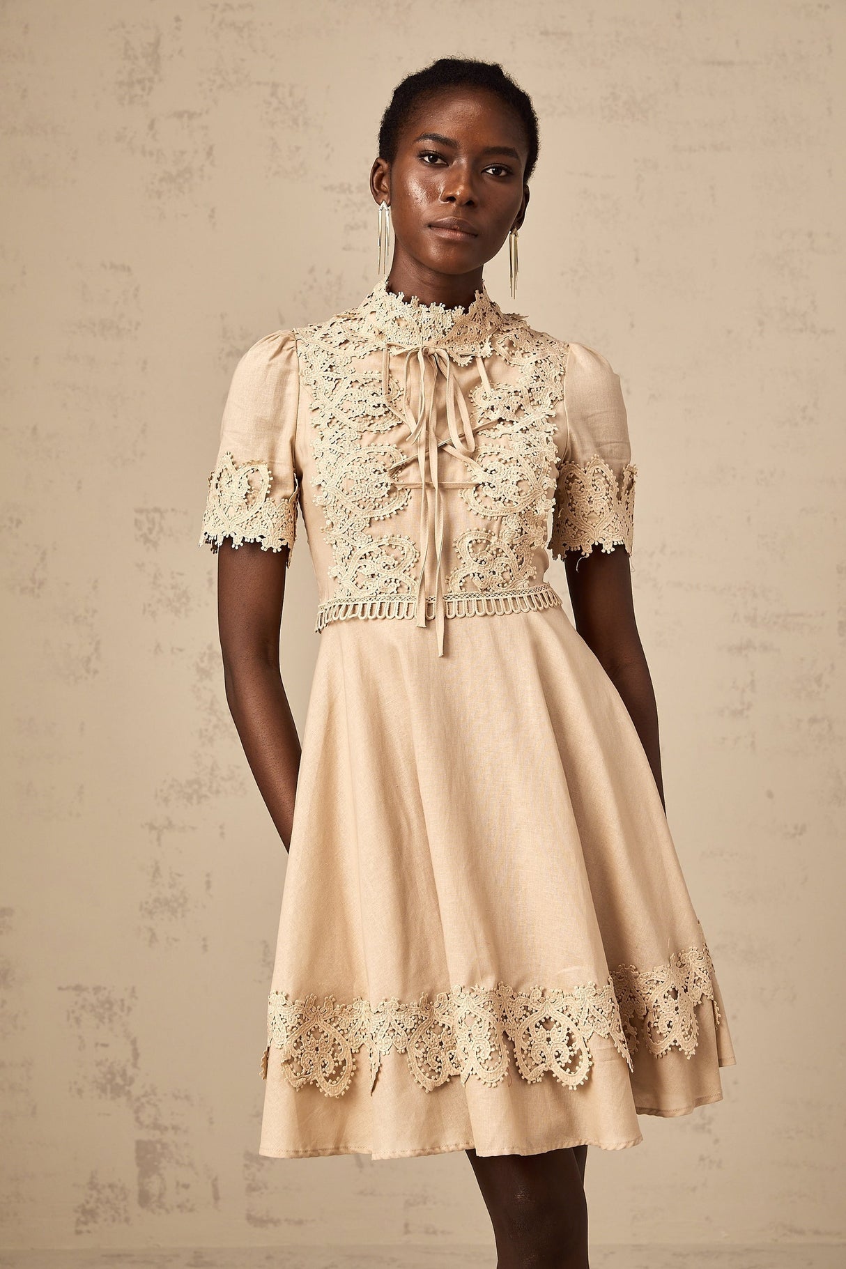 Young woman wearing a short flared dress with corded lace pattern and delicate straps standing against a plain background